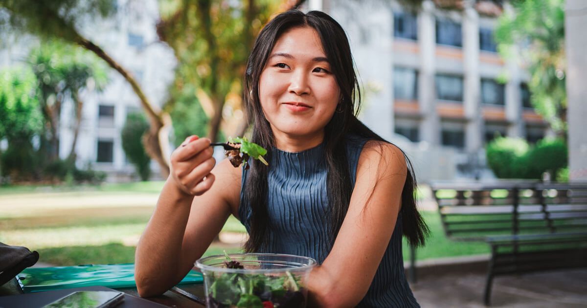 Person Smiling While Holding a Fork Over a Salad — Trinity Beach Dental In Trinity Beach, QLD