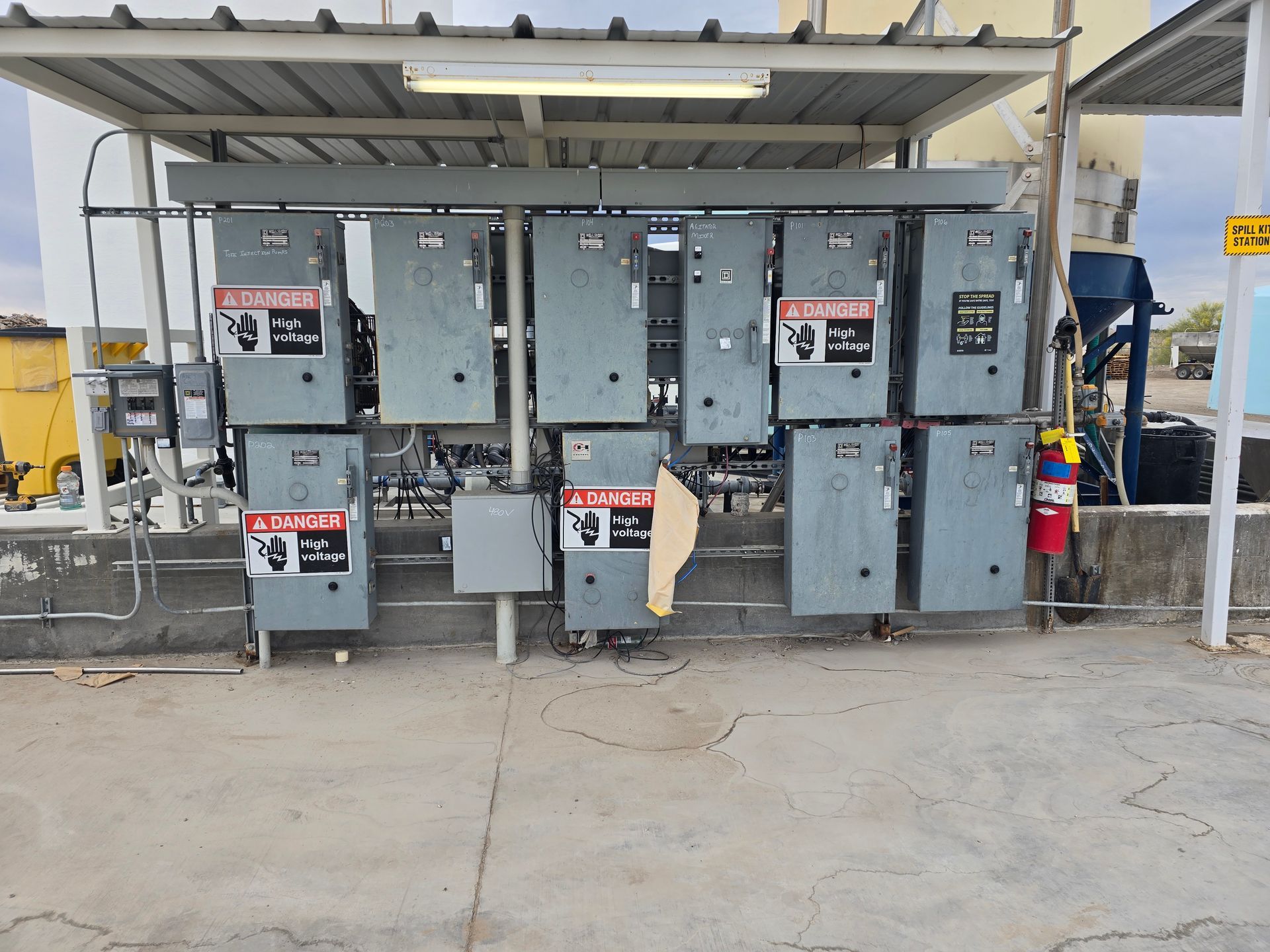 Gray electrical panels mounted on a wall beneath a metal canopy; warning signs are visible.