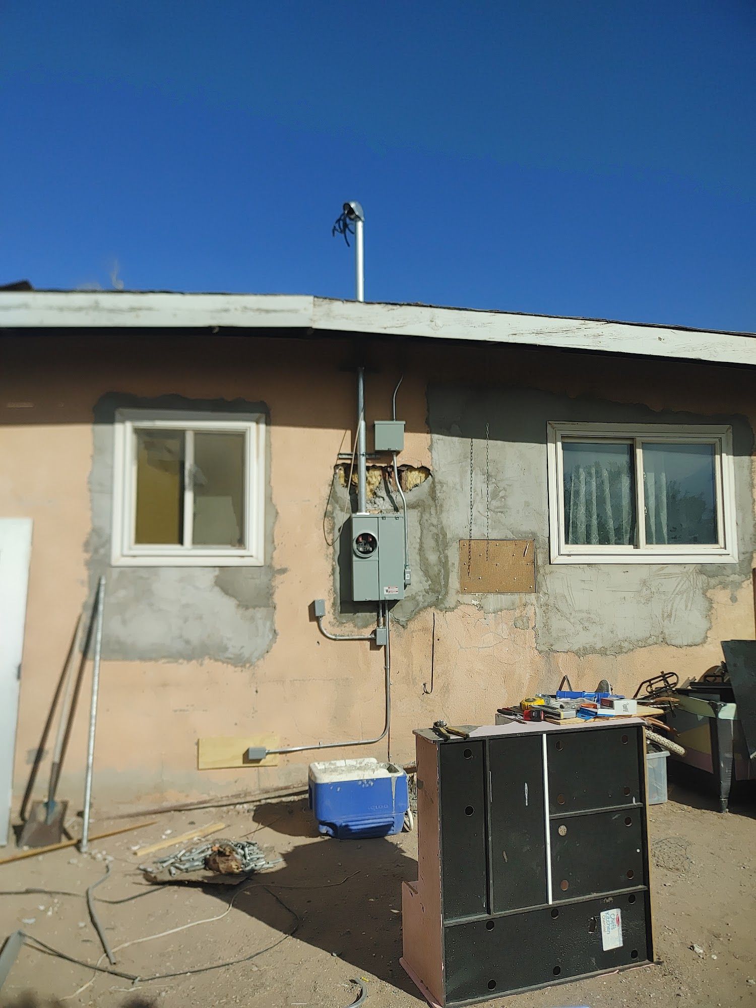 Exterior view of a stucco building with electrical equipment and a vent pipe extending above the roof.