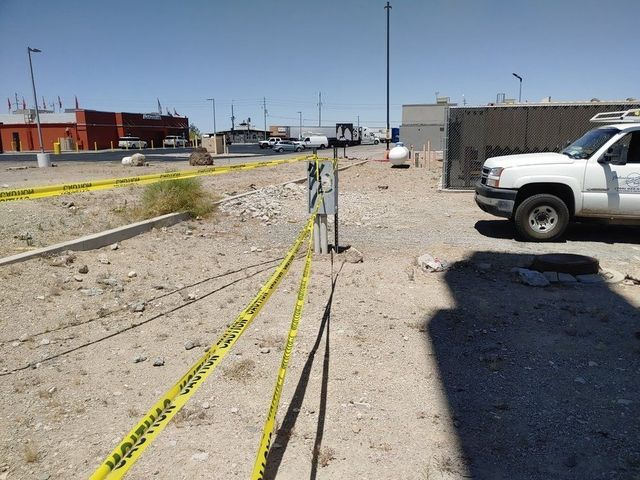 A work site with caution tape, truck, and surveying equipment in a gravel lot on a sunny day.