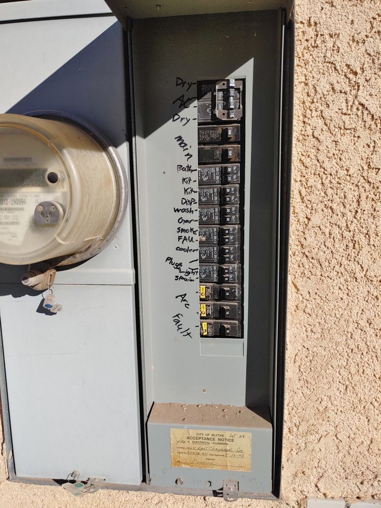 Electrical panel with circuit breakers, labeled with black marker, next to a meter.