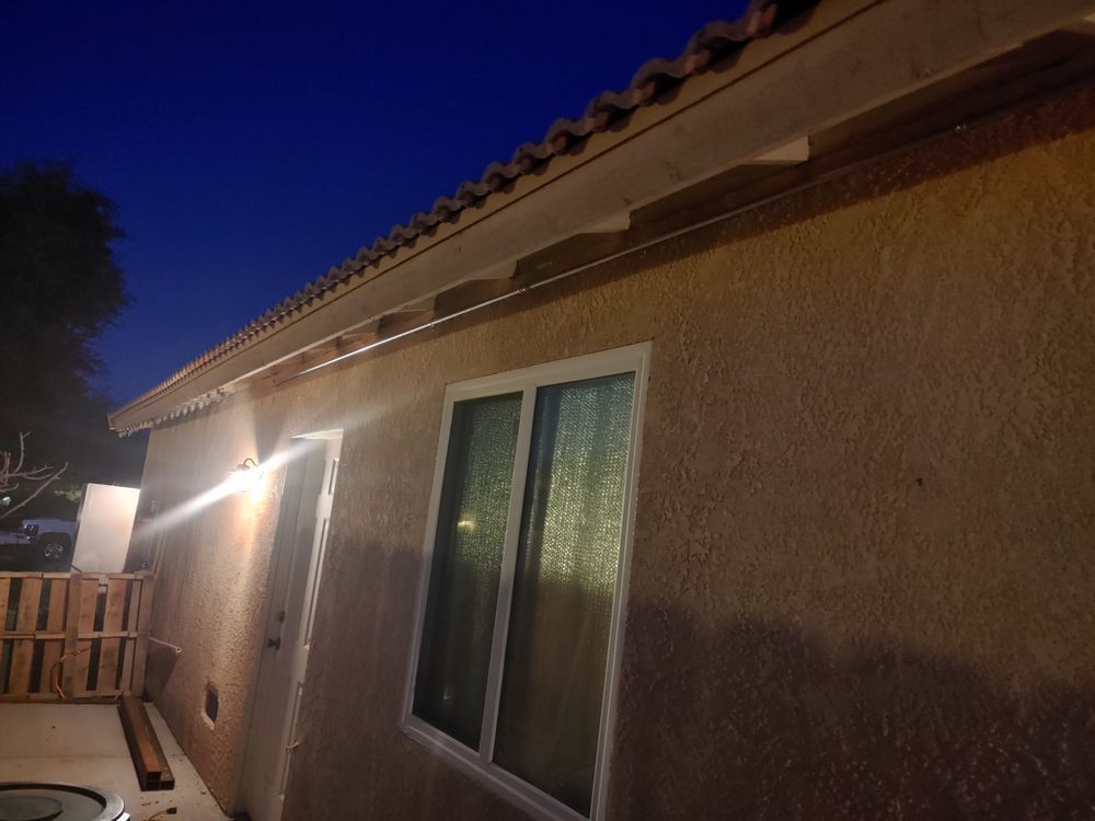 Tan stucco house exterior with a window, eaves, and a dark blue sky.