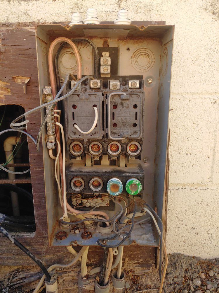 An old, exposed electrical fuse box with visible wiring and empty fuse sockets on a weathered wall.
