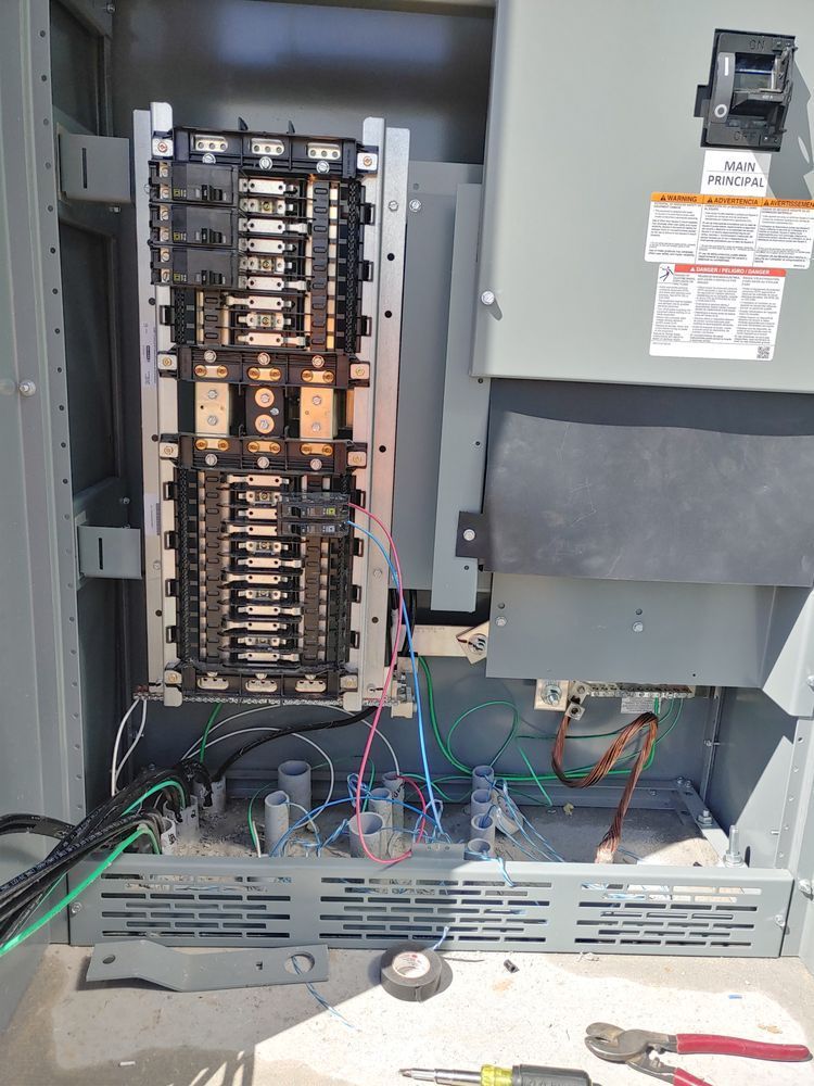 Electrical panel with circuit breakers and wiring exposed. Gray enclosure, tools below.
