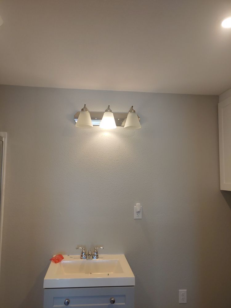 Bathroom with a three-light fixture above a sink and cabinet. Walls are gray.