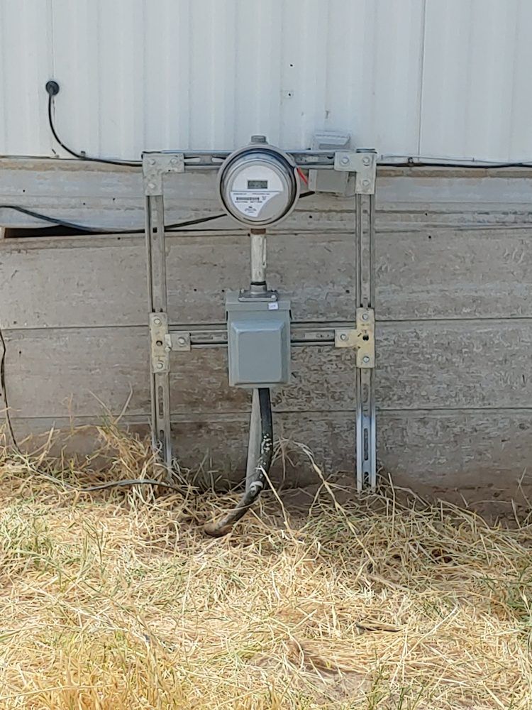 Utility meters mounted on a light gray siding of a building, with dry grass in the foreground.