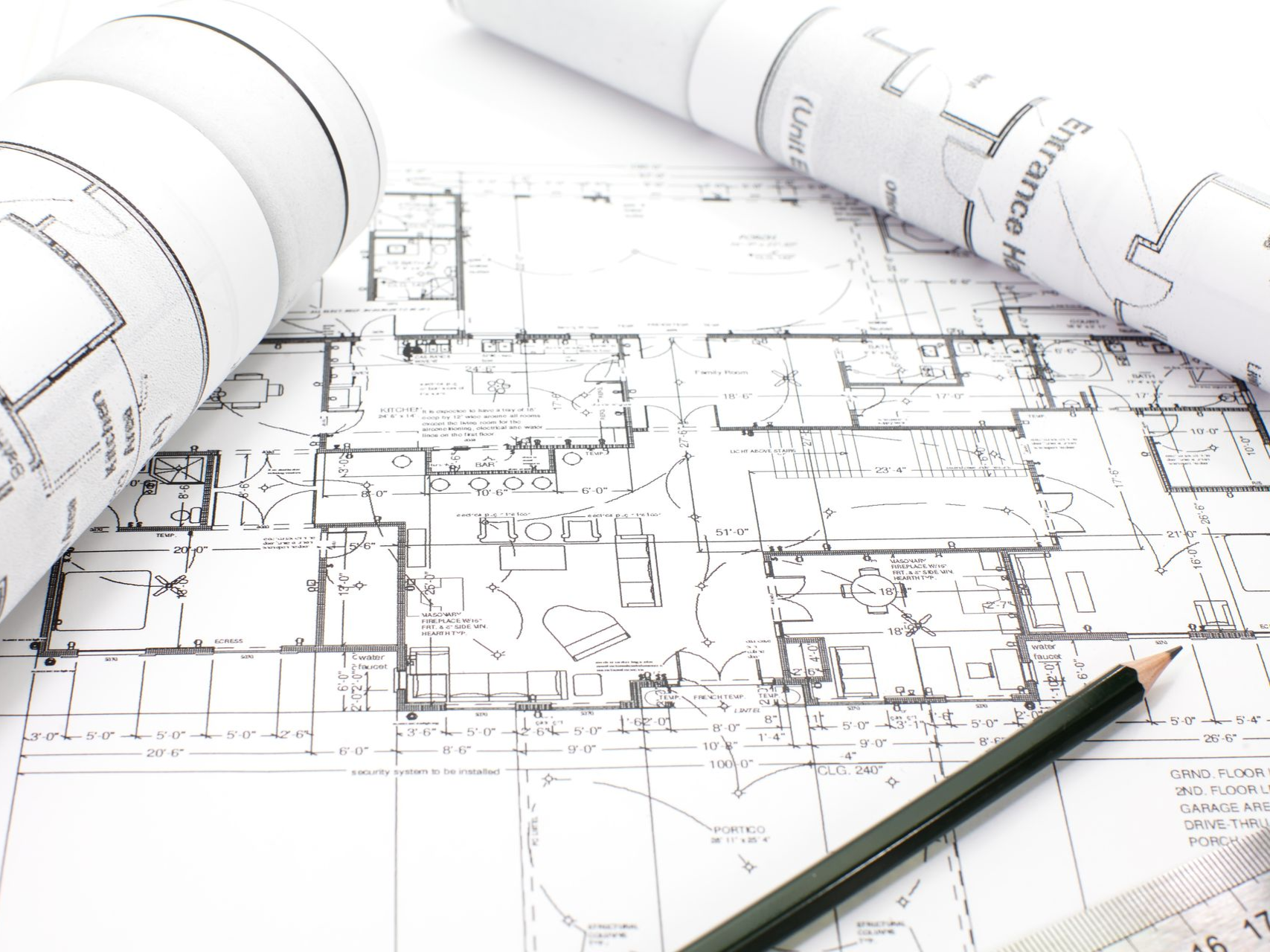 Architectural blueprints with rolled-up plans and a pencil on a white surface.