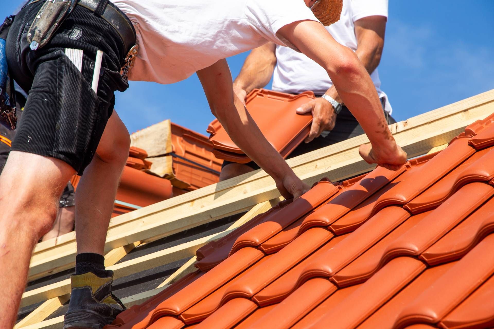 Workers installing red roof tiles on a house roof under a blue sky
