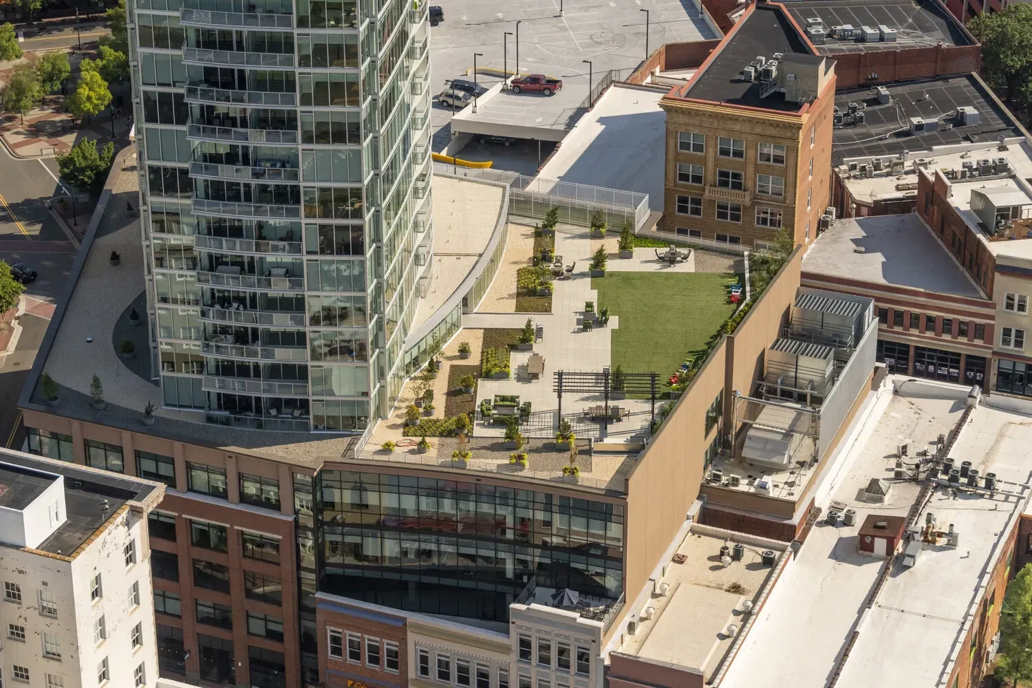 Aerial view of a modern apartment building with a rooftop terrace featuring lounge seating, tables, and a green lawn area.