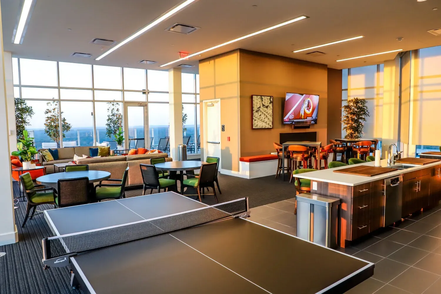 Modern lounge area with ping pong table, kitchen island, bar seating, and city views.