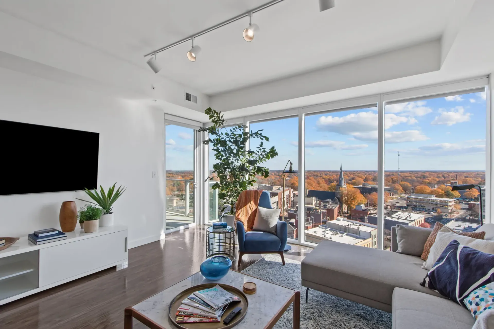 Living room with a sectional couch, armchair, coffee table, and large windows with a city view.
