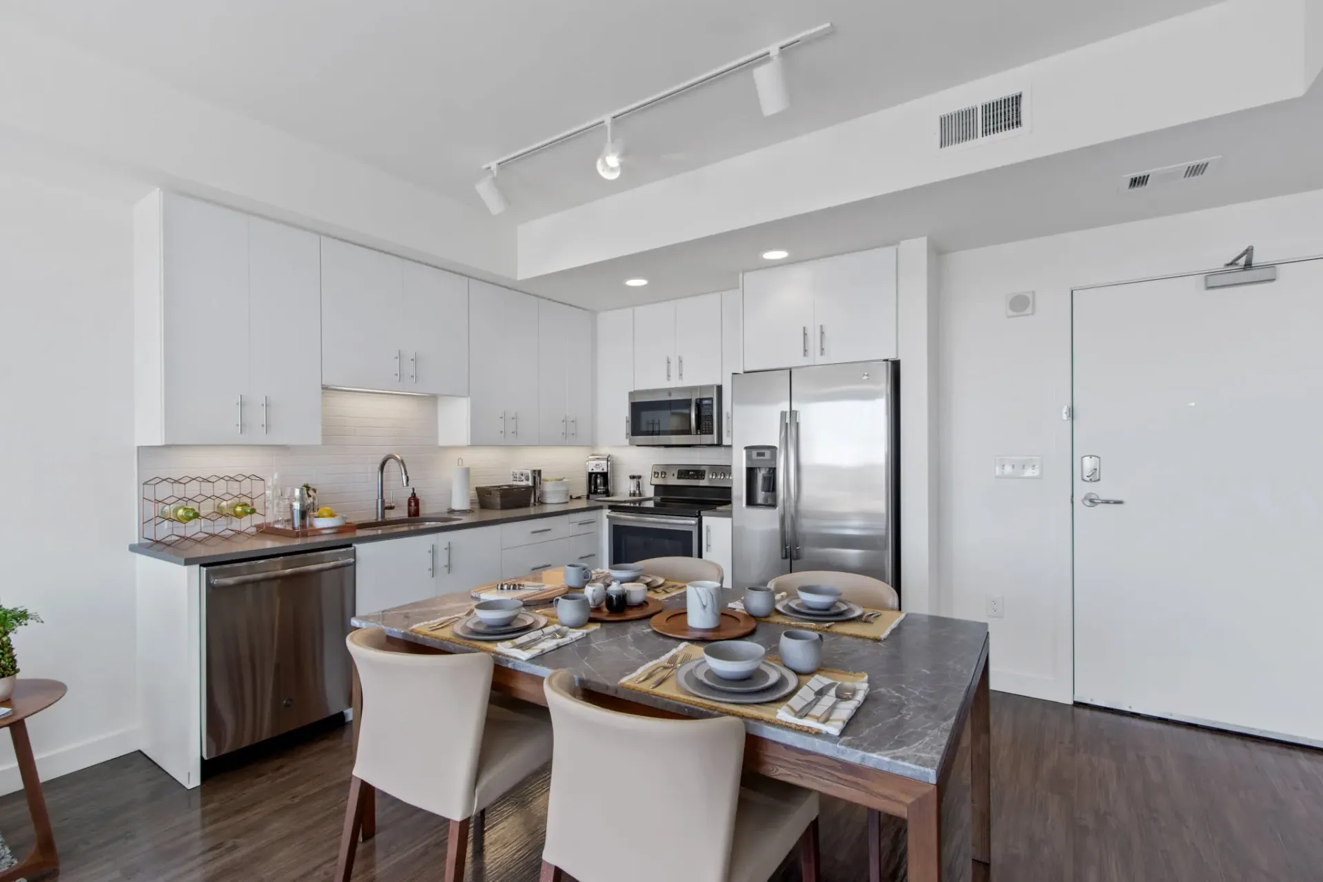 Modern kitchen with a dining table set for four, stainless steel appliances, and white cabinetry.