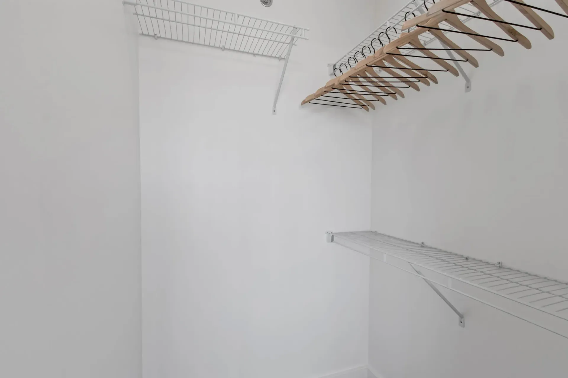 Empty walk-in closet with white wire shelving and wooden hangers.