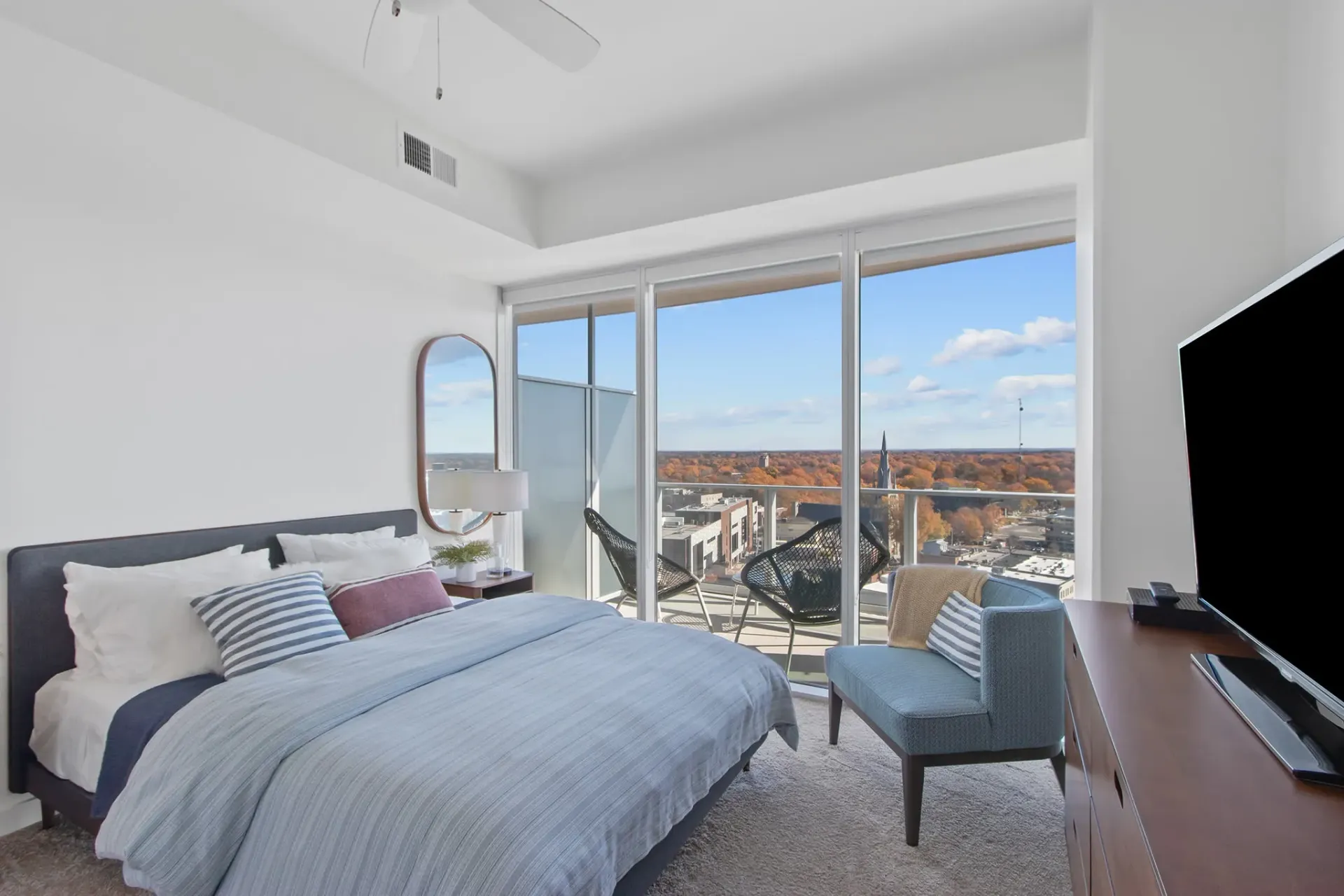 Bedroom with a large bed, a television, and a balcony with a city view.