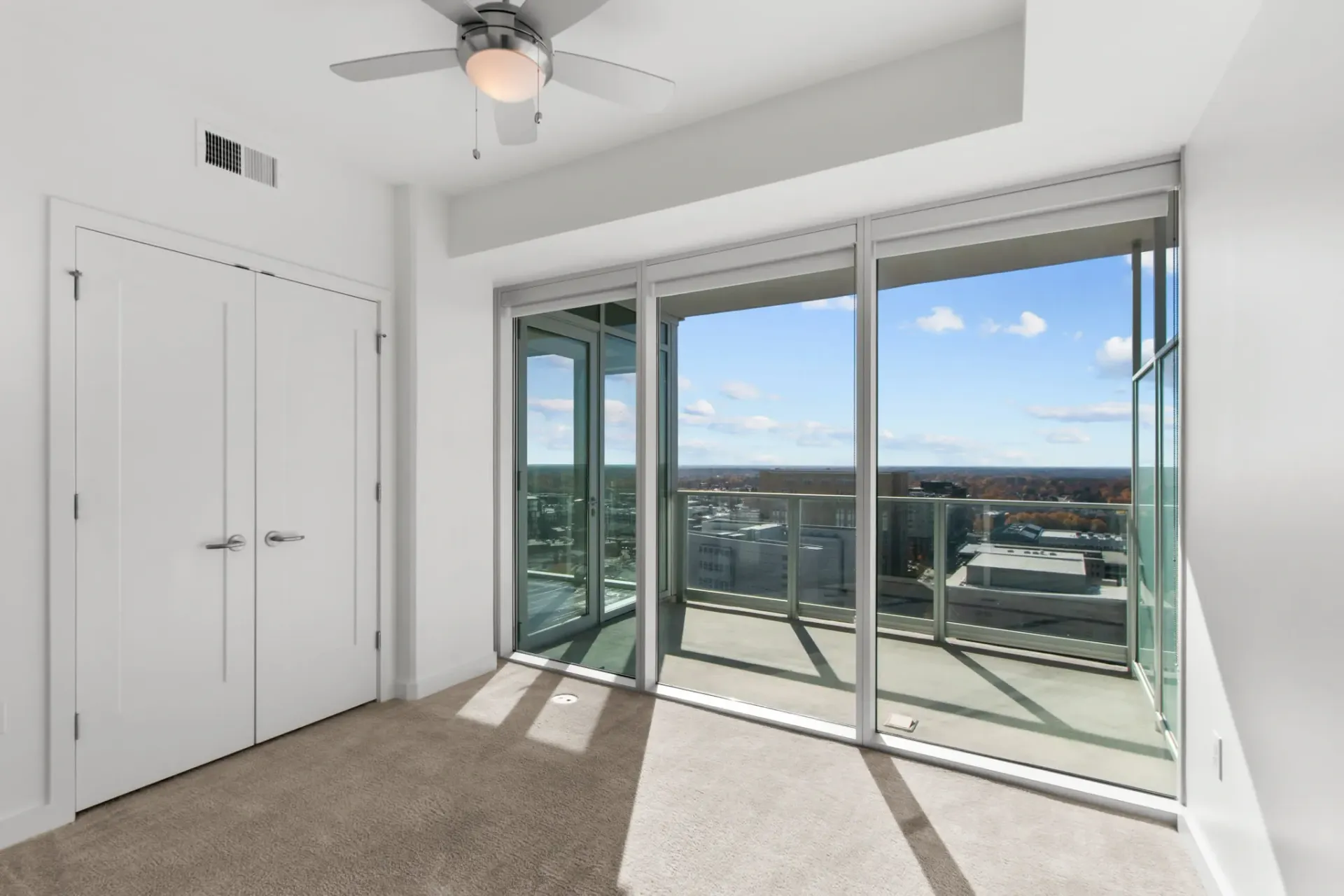 Bedroom with ceiling fan and large balcony overlooking the city
