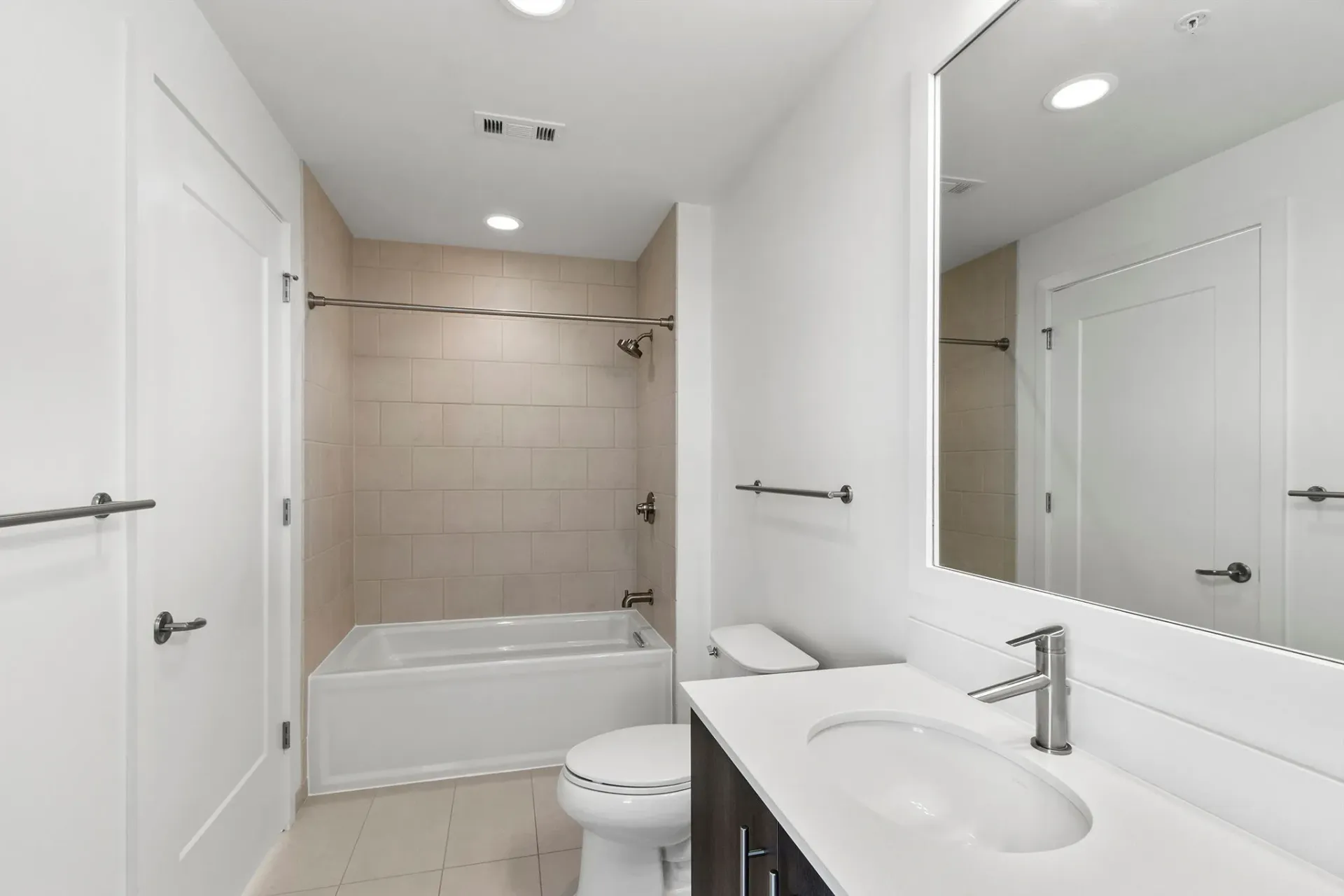 Modern bathroom with a white vanity, sink, toilet, and bathtub with tiled shower walls.
