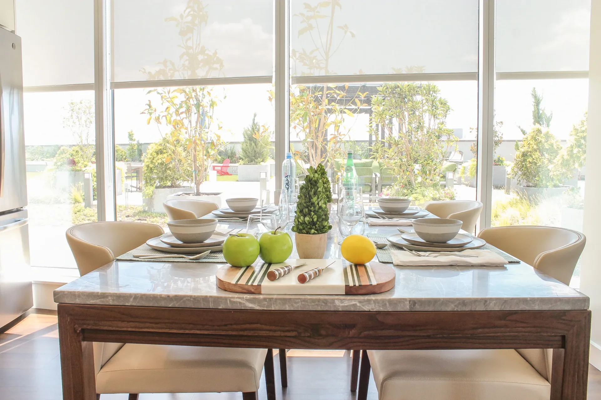 A dining table set for four with apples and a lemon on a marble tabletop.