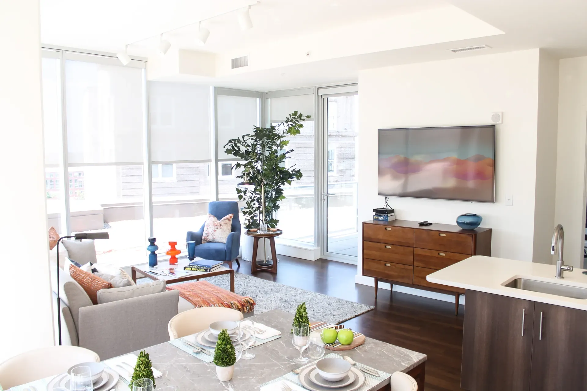 Modern living room with a dining area, featuring a sofa, armchair, TV, and a balcony.
