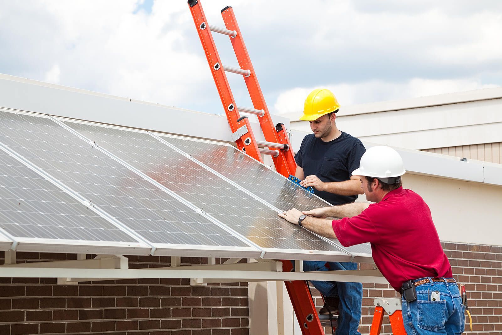 Two workers installing solar panels on a roof, with orange ladders and hard hats