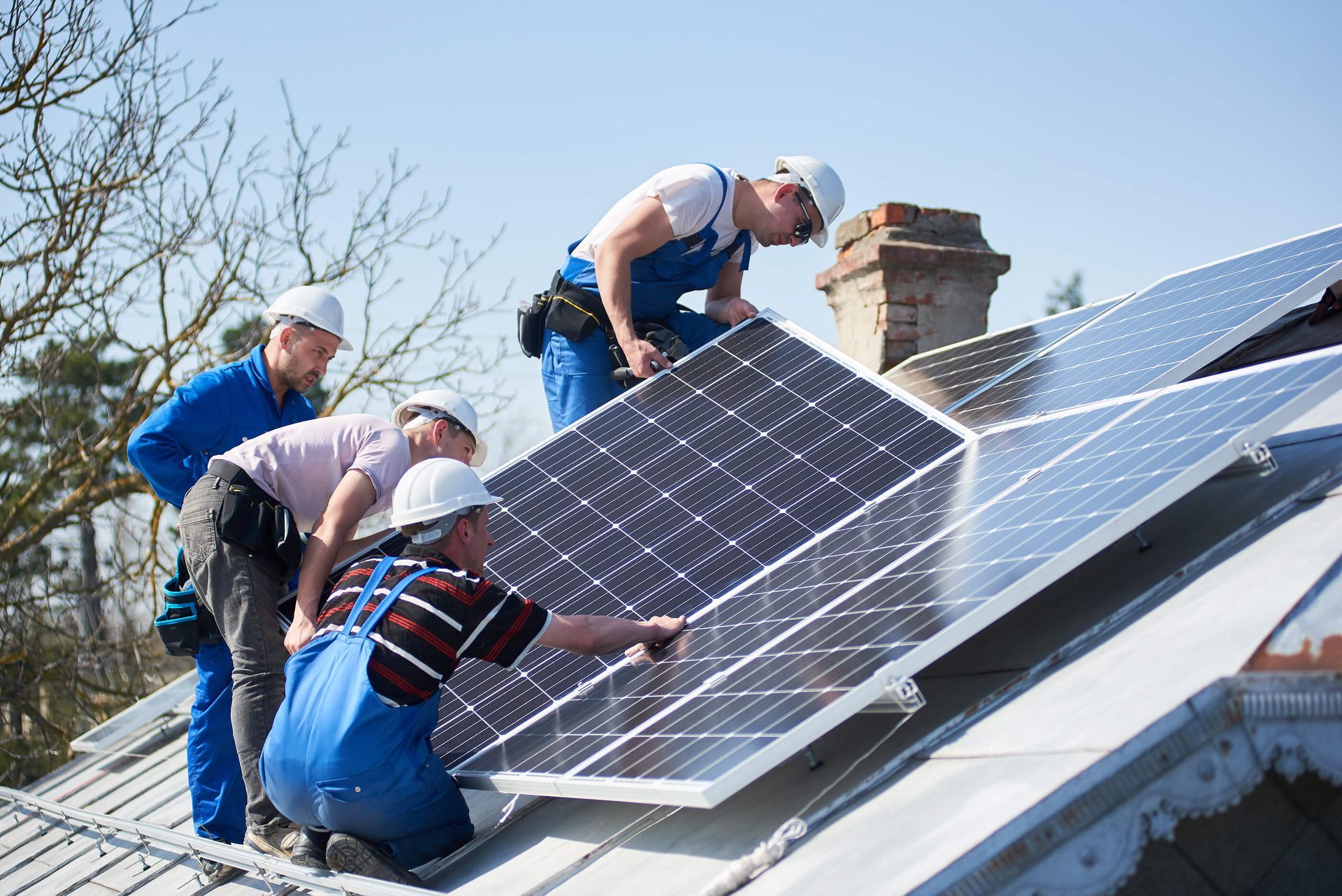 Workers installing solar panels on a rooftop under a clear blue sky