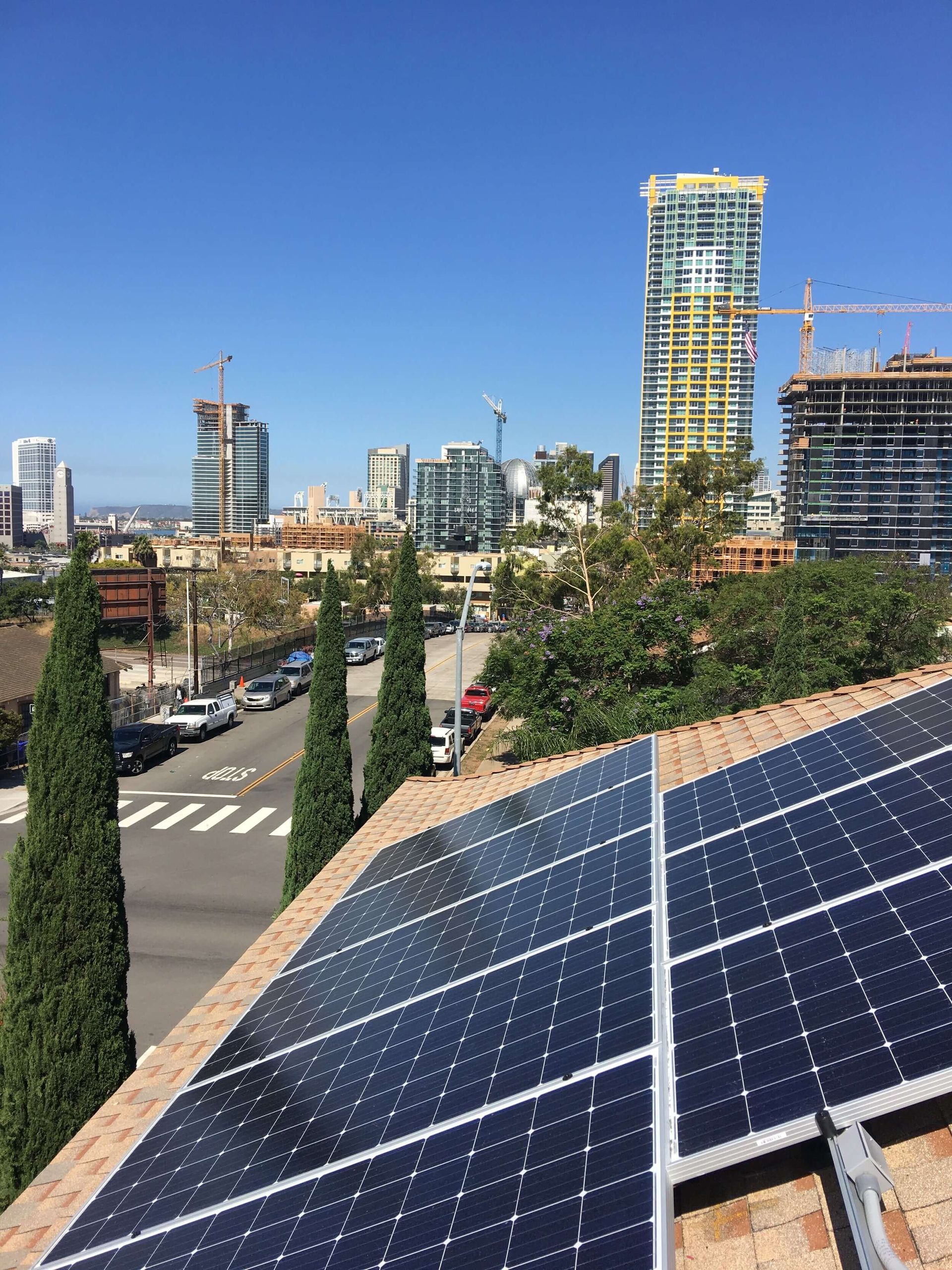 Solar panels on a rooftop overlooking a city skyline under a clear blue sky.