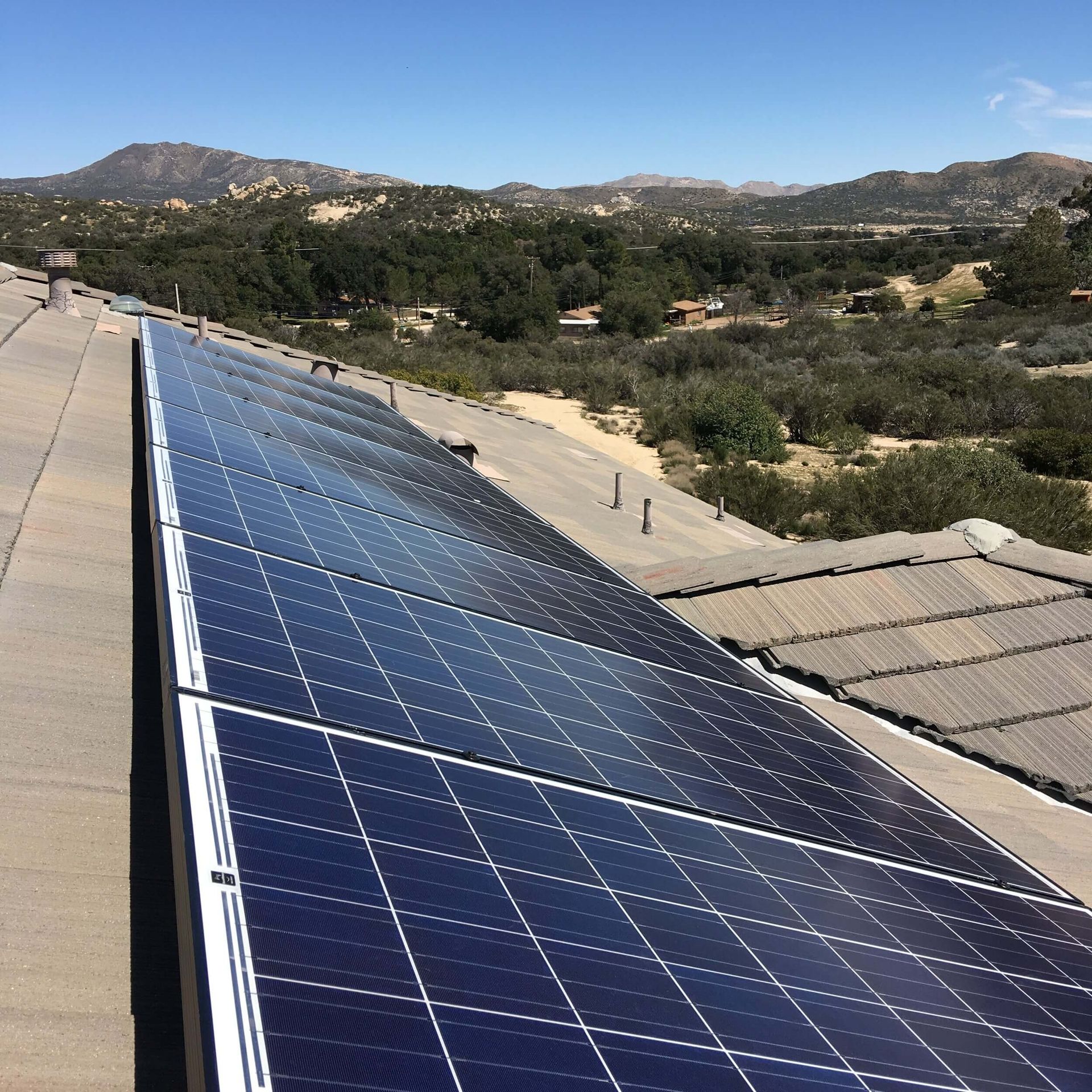 Solar panels on a rooftop overlooking a dry landscape with hills and trees