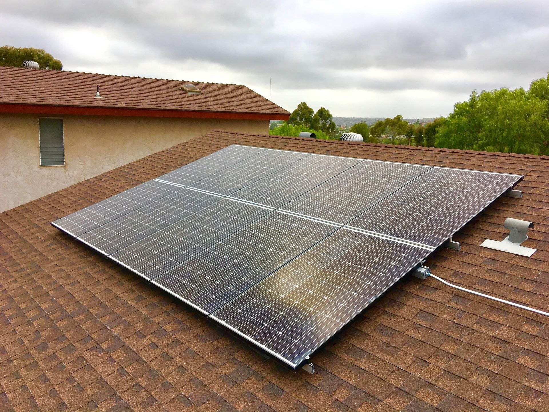 Solar panels mounted on a brown tiled rooftop under a cloudy sky.