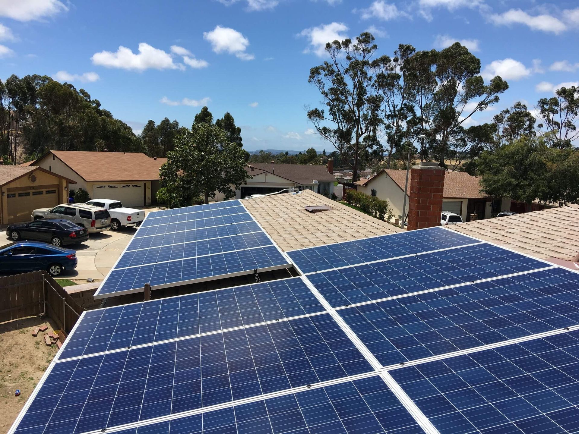 Solar panels on a rooftop in a suburban neighborhood under a blue sky.