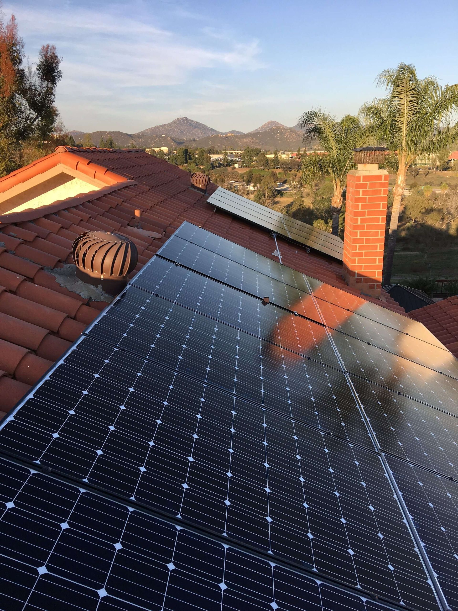 Solar panels on a rooftop at sunset with a chimney and distant hills.
