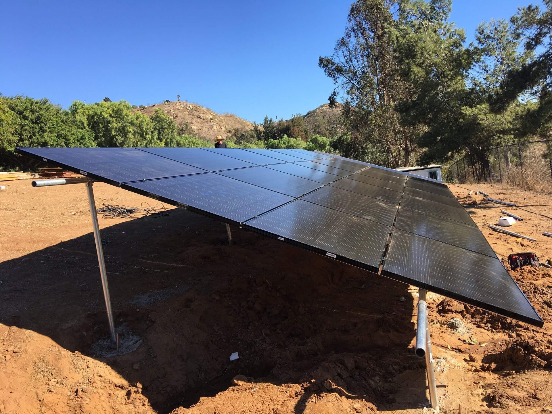 Solar panels on a tilted array in a dry, rural landscape under a clear blue sky.
