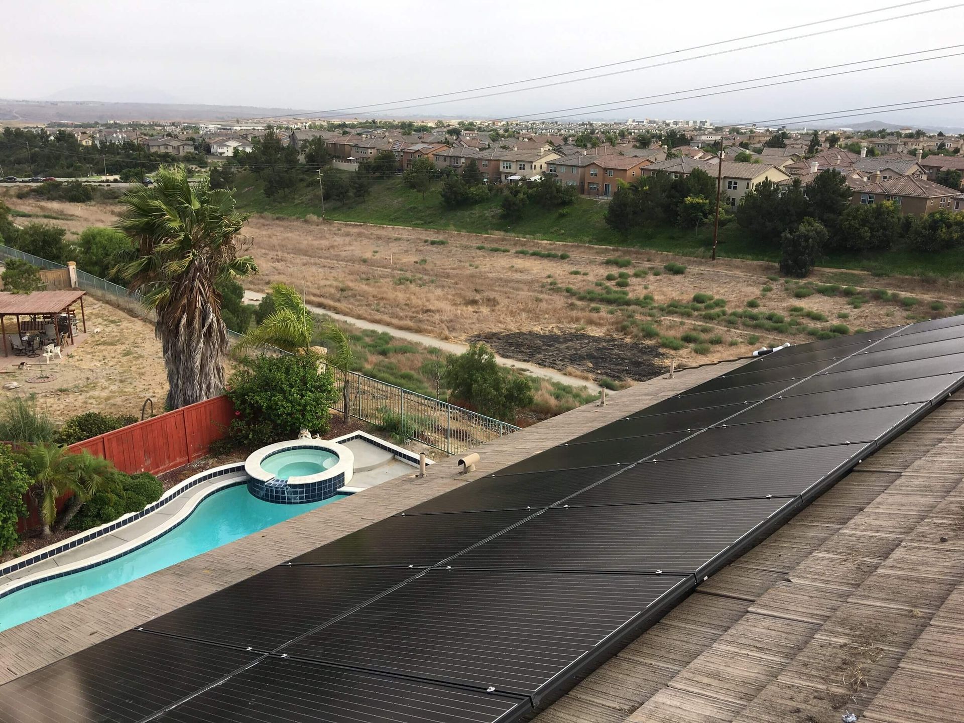 Rooftop solar panels beside a backyard pool overlooking a dry, open landscape