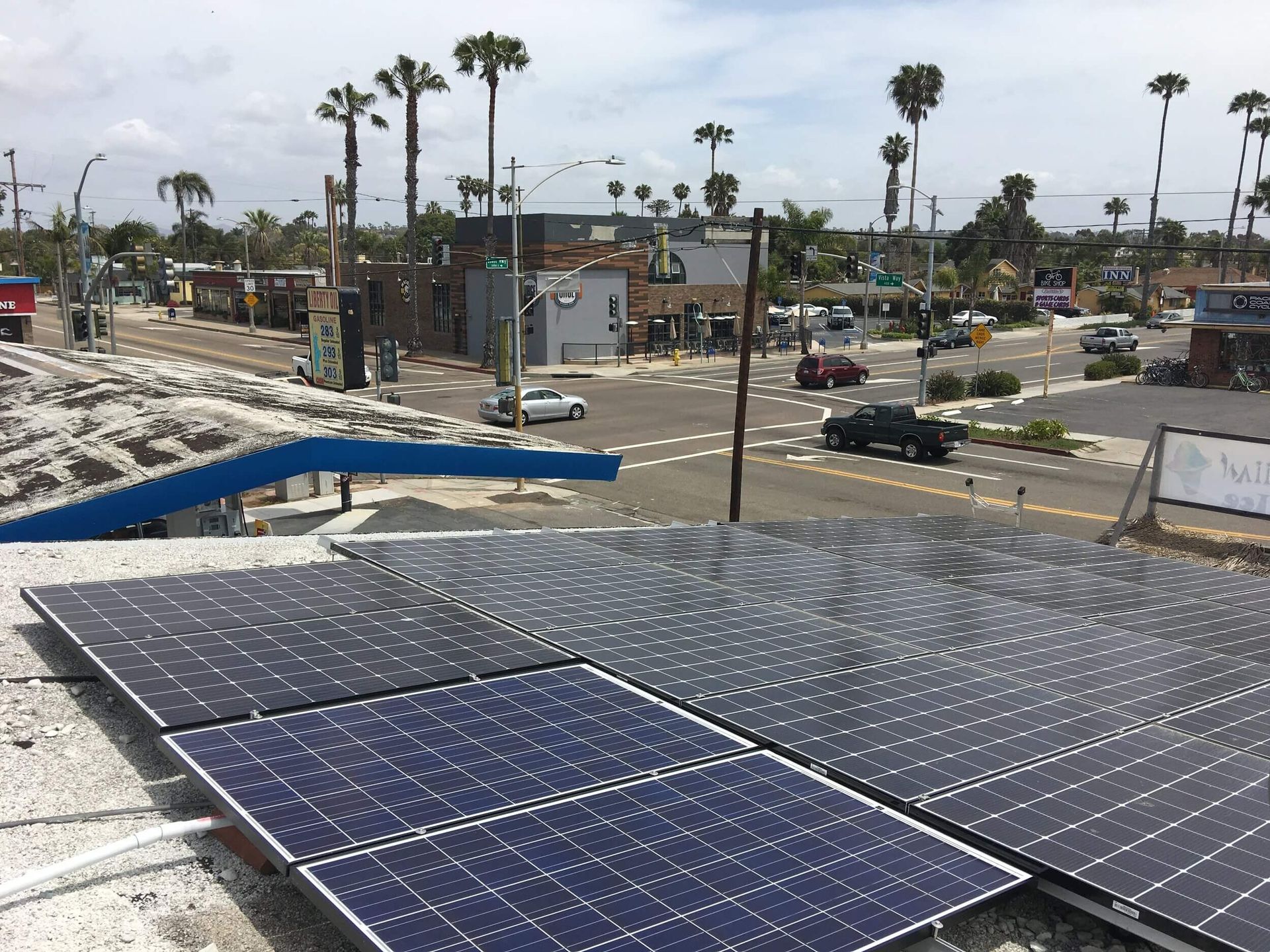 Solar panels on a rooftop overlooking a palm-lined street and houses under a clear sky.
