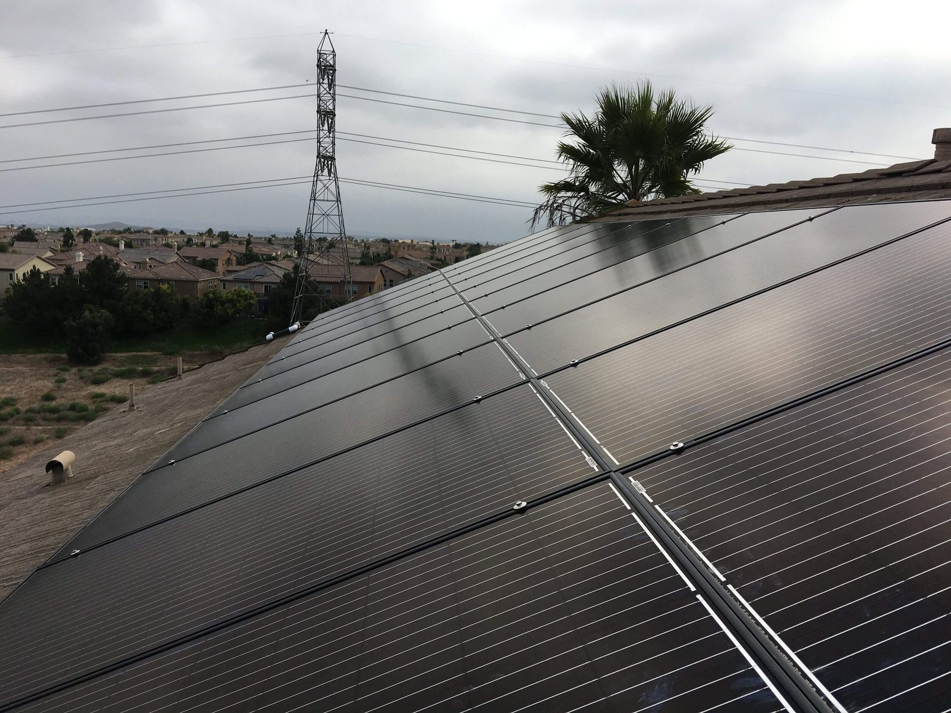 Solar panels on a rooftop under a cloudy sky, with a power line tower in the background.