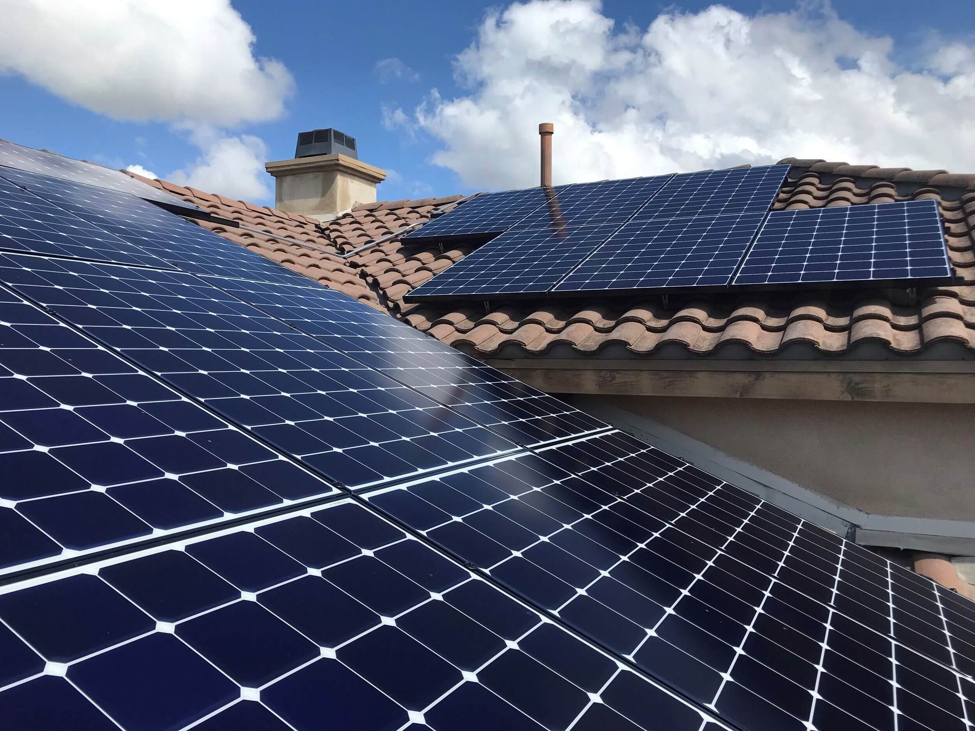 Solar panels on a tiled roof under a blue sky with clouds