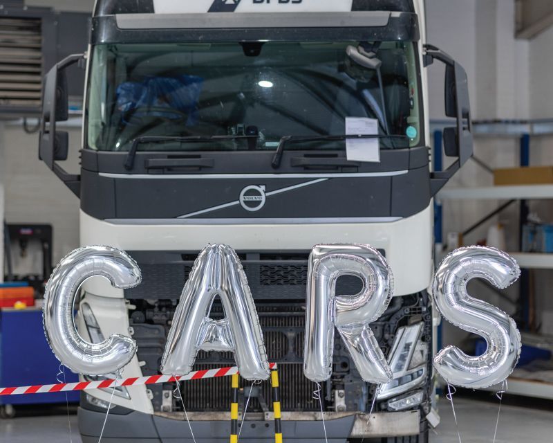 Silver balloons spelling out 'CARS' in front of a Volvo truck.