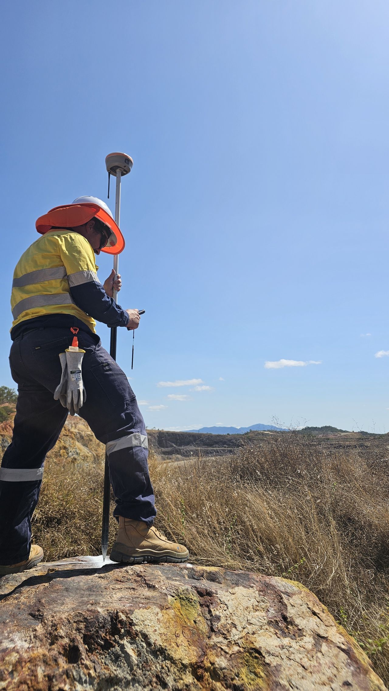 Worker in orange hard hat and reflective vest surveying a rocky landscape under a clear blue sky. — UAScend Aerial Solutions in Townsville, QLD