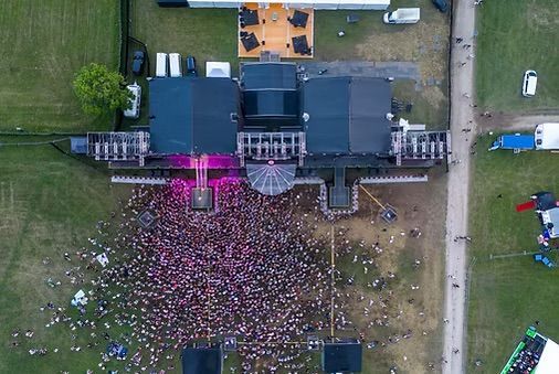Aerial view of a large crowd gathered before a stage with pink lights in a grassy outdoor venue — UAScend Aerial Solutions in Townsville, QLD