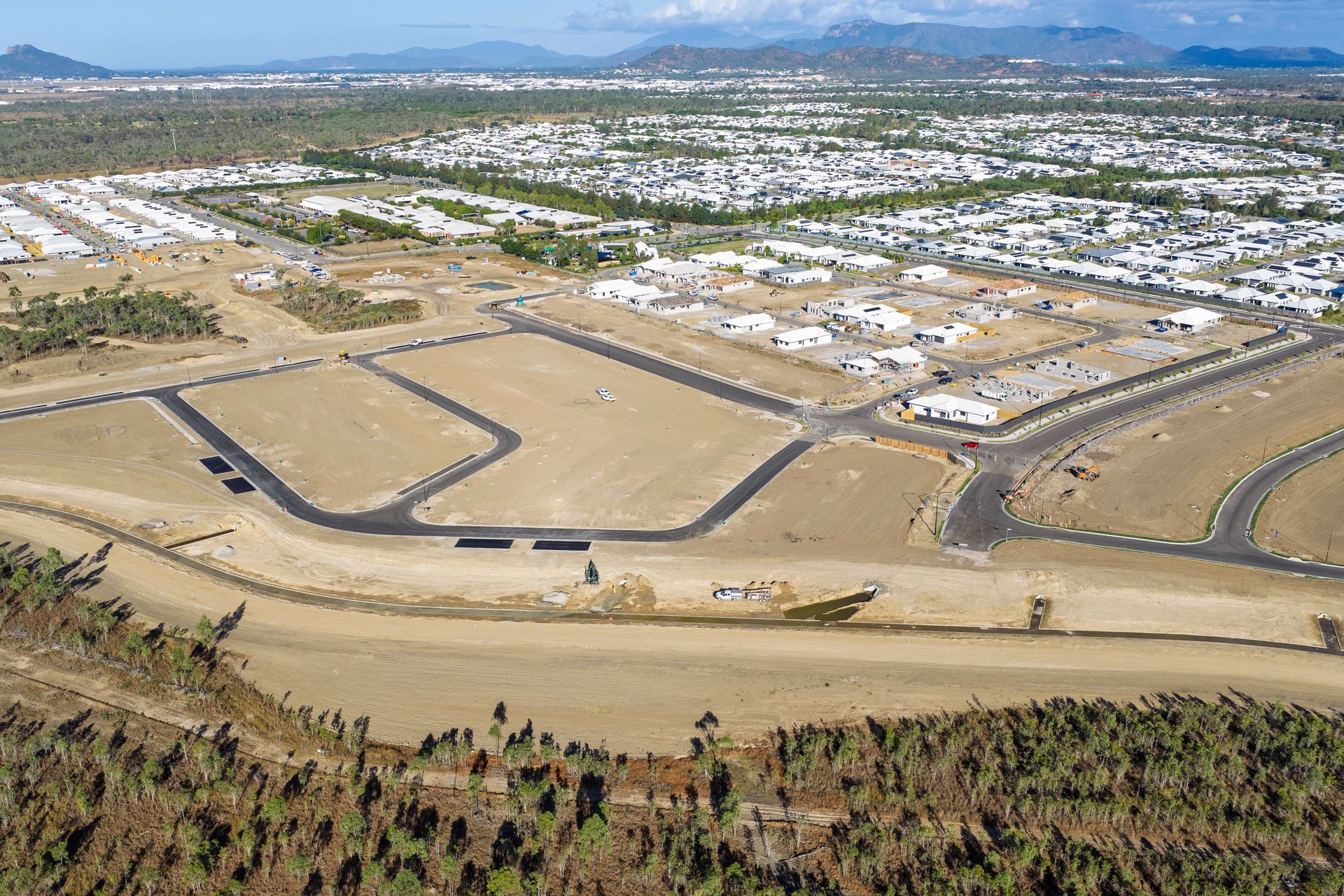 Aerial view of a new housing development beside a dirt road, with mountains in the background. — UAScend Aerial Solutions in Townsville, QLD