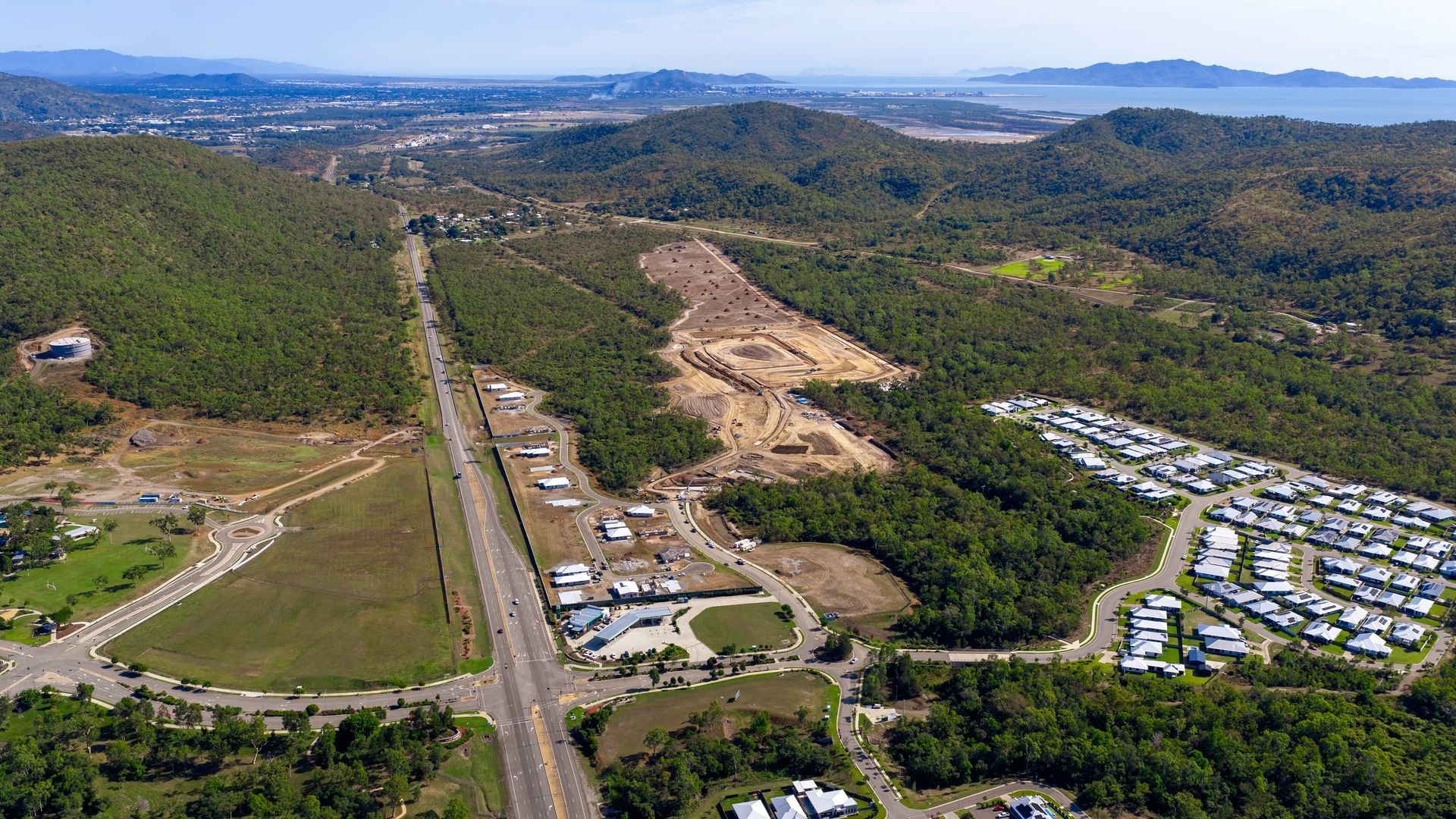 Aerial view of a cleared hillside near a highway, with green forest, scattered homes, and distant coastline. — UAScend Aerial Solutions in Townsville, QLD