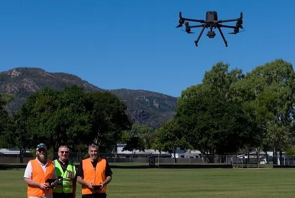 Three Workers in Orange Vests Watch a Drone Flying — UAScend Aerial Solutions in Townsville, QLD