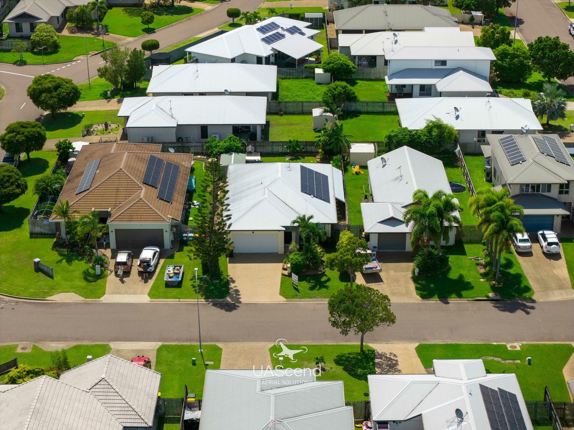 Aerial view of suburban houses with white roofs and solar panels along a tree-lined street — UAScend Aerial Solutions in Townsville, QLD