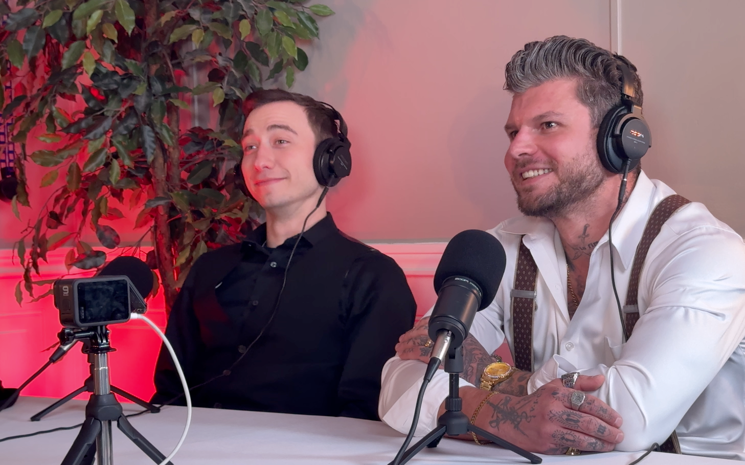 Isadore Goldsein and Alex Donnolo wearing headphones, seated at a table with microphones, recording a podcast.