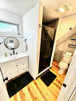 Bathroom with white vanity, black accents, glass shower, and wood floor.