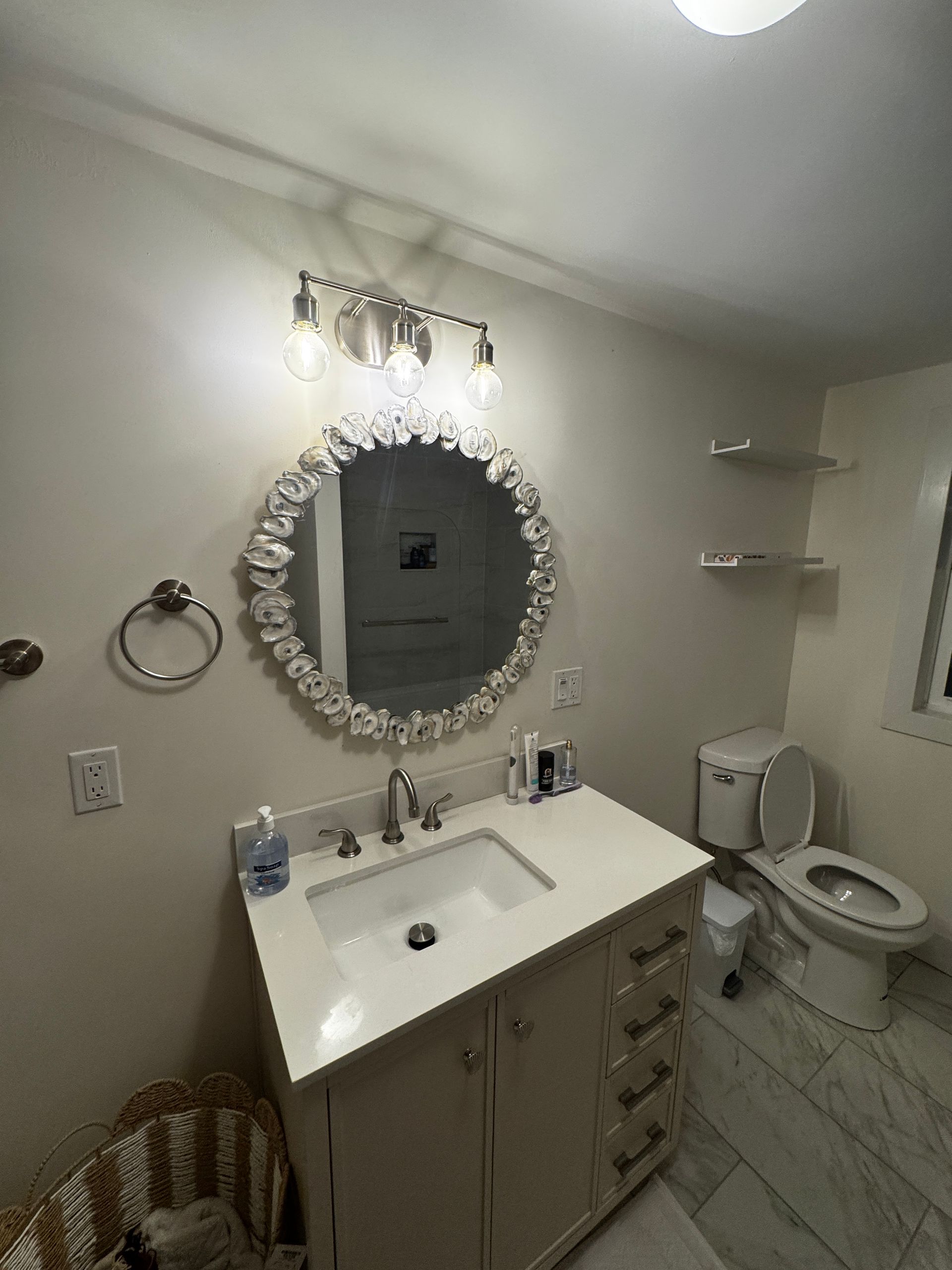 Bathroom with a white vanity, a round mirror with a decorative frame, and a toilet.