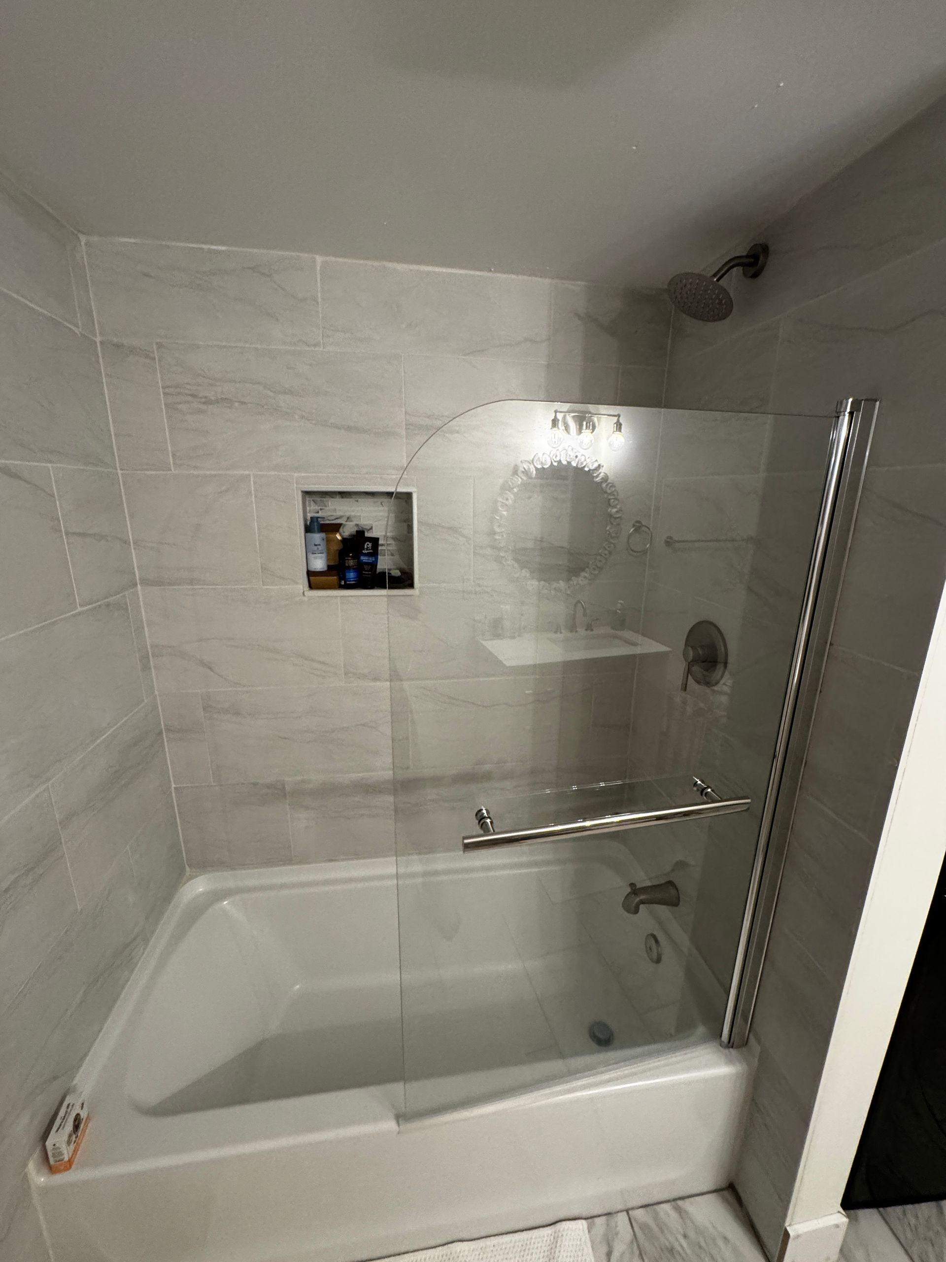 Bathroom with a white bathtub, glass shower door, and light gray tiled walls.