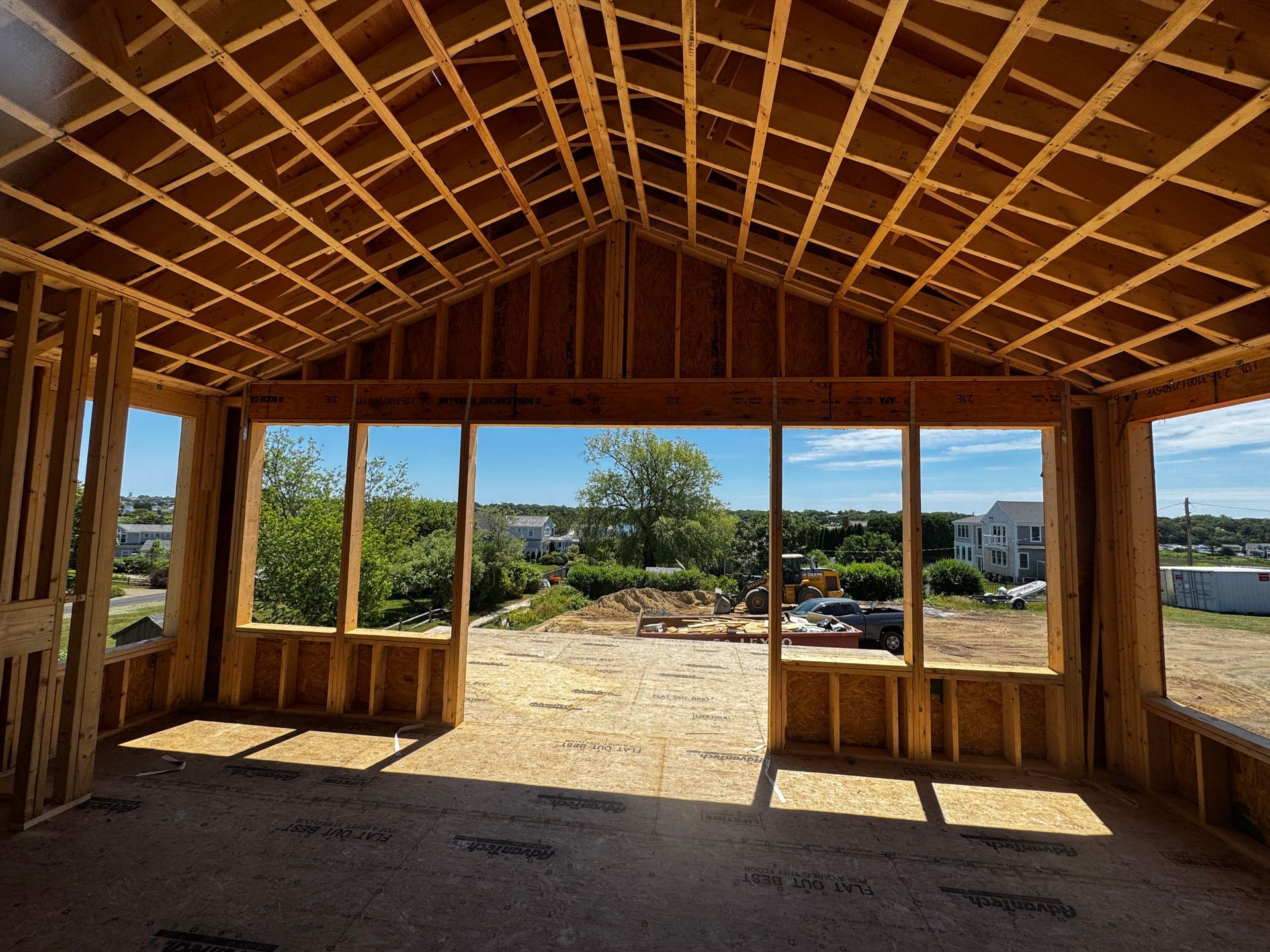 Interior view of a building under construction, framed with wooden beams, with a view of the outside.