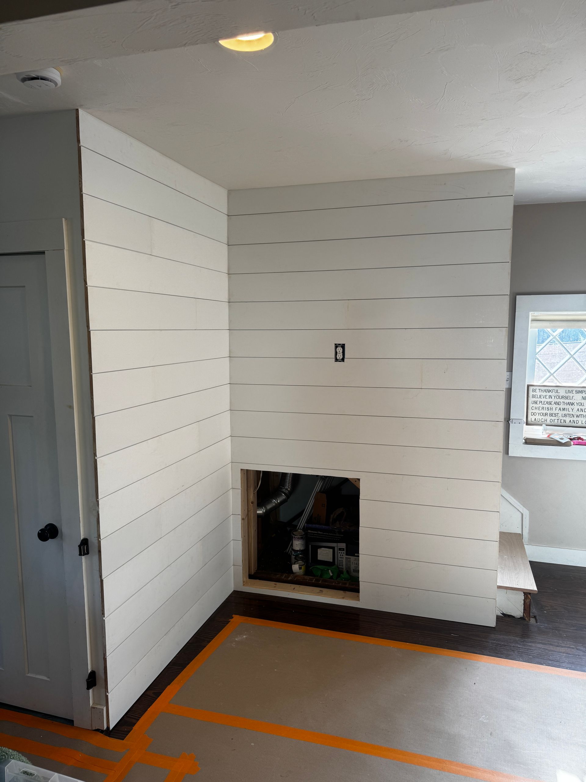 Interior room with a shiplap wall and a recessed fireplace opening, unfinished construction.