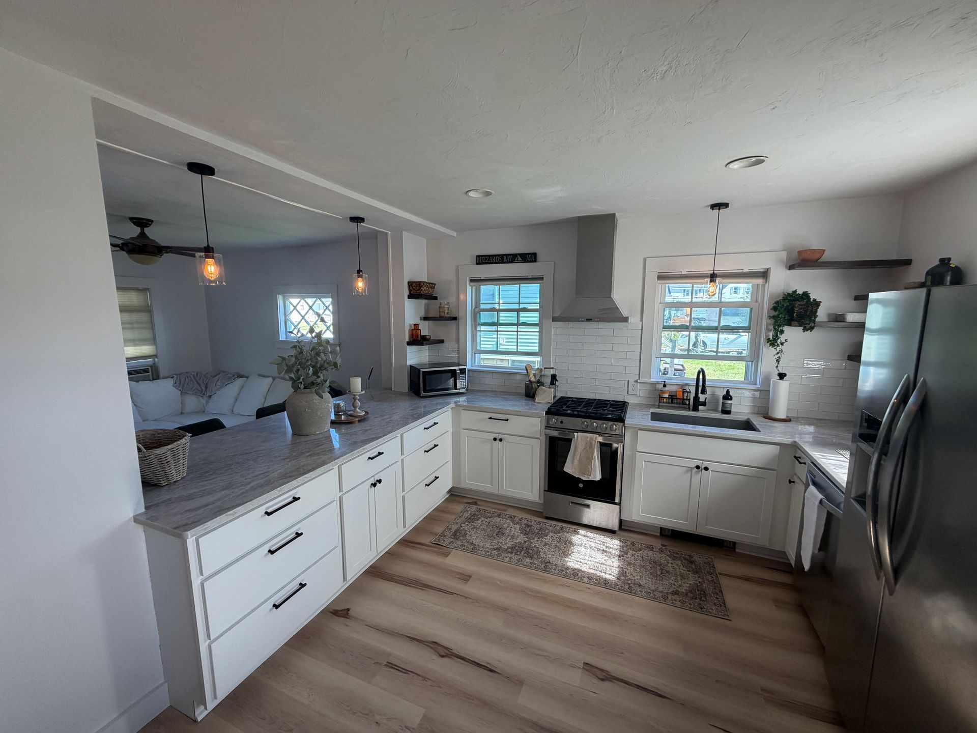 Bright, white kitchen with gray countertops, stainless steel appliances, and wooden flooring.