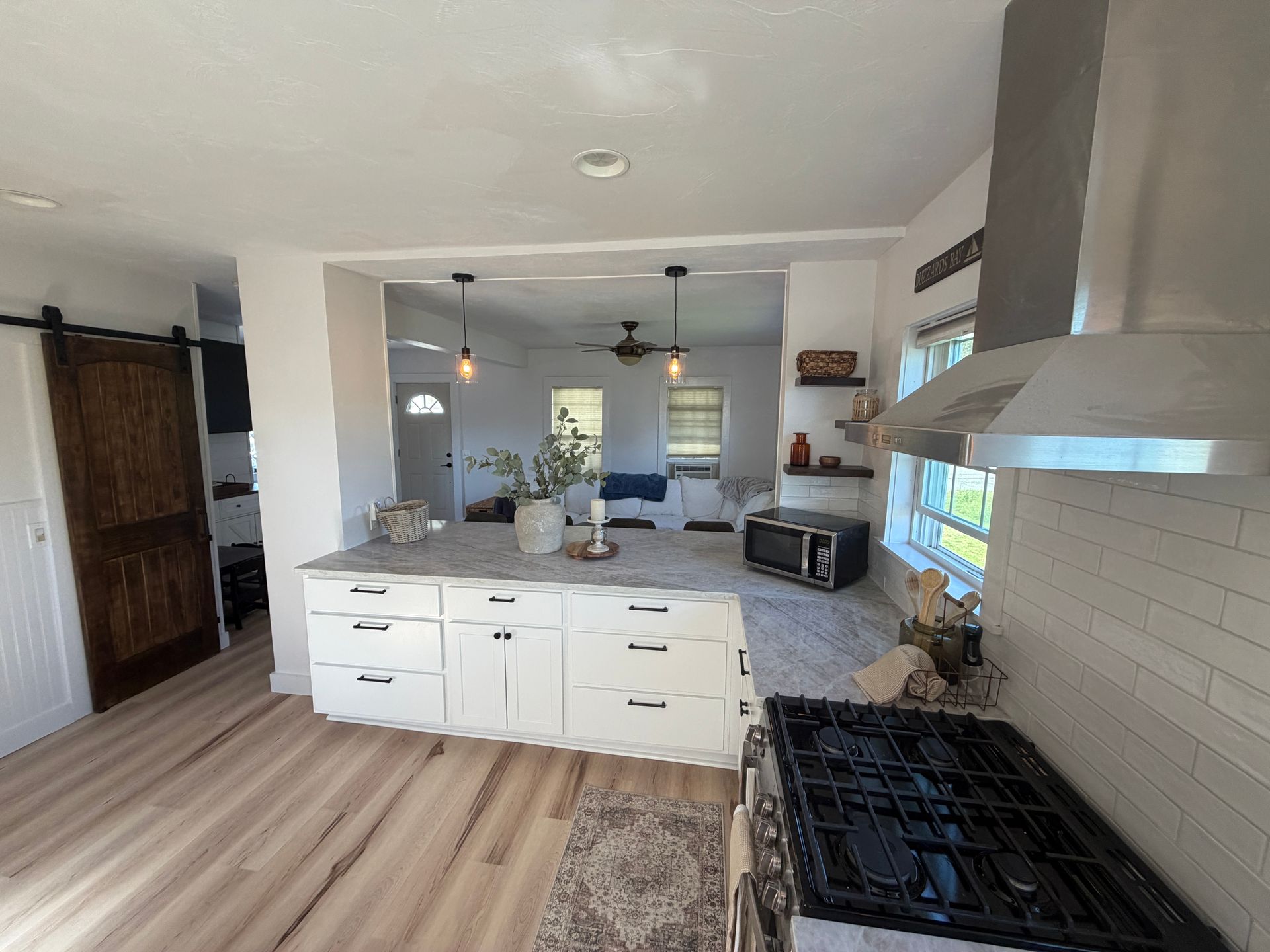 Kitchen with white cabinets, gray countertops, and stainless steel range hood. Open to a living area.
