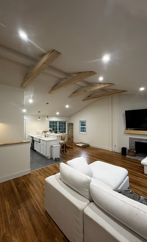 Living room with wood beams on the ceiling, white sofa, hardwood floors, and a fireplace.